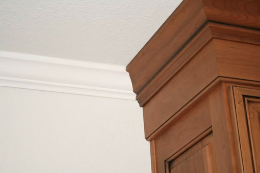 Detail view of a ceiling corner showing crown molding and a wood cabinet.