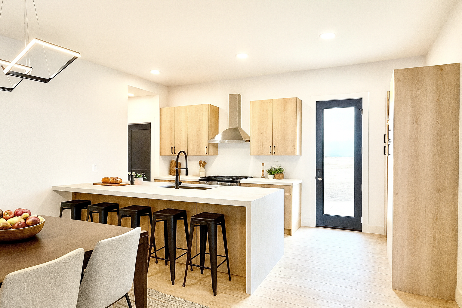 Light-filled, modern kitchen with warm wood cabinetry, white surfaces, and clean black accents.