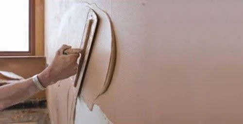 Detail view of a person sanding a curved interior wall near a window.