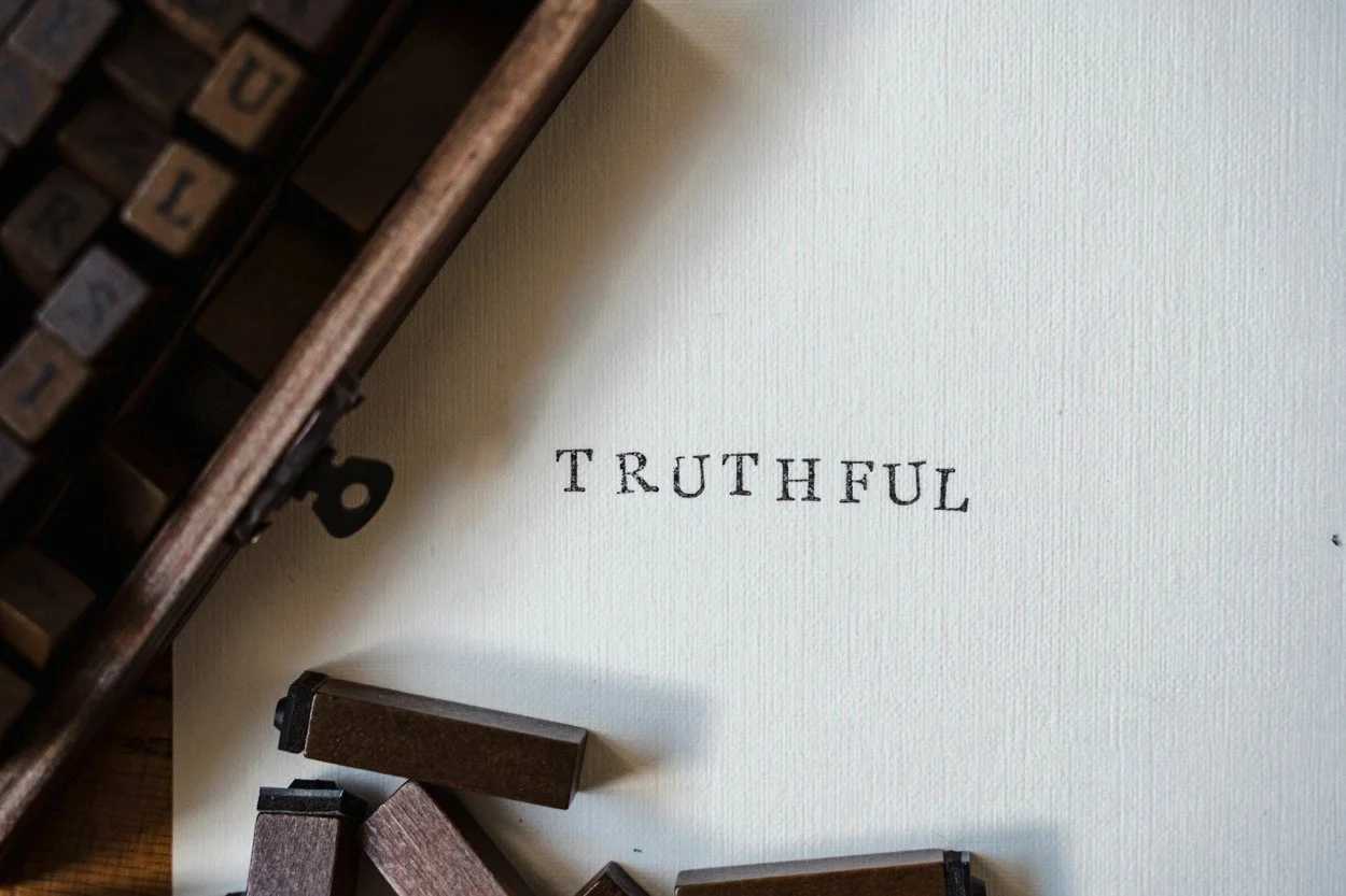 A vintage typewriter with scattered alphabet tiles on a table, spelling the word 'TRUTHFUL' on a piece of paper.