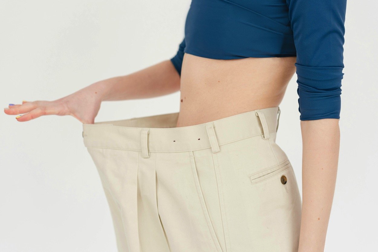 Person wearing oversized white pants, holding out the waistband to show it's too large.