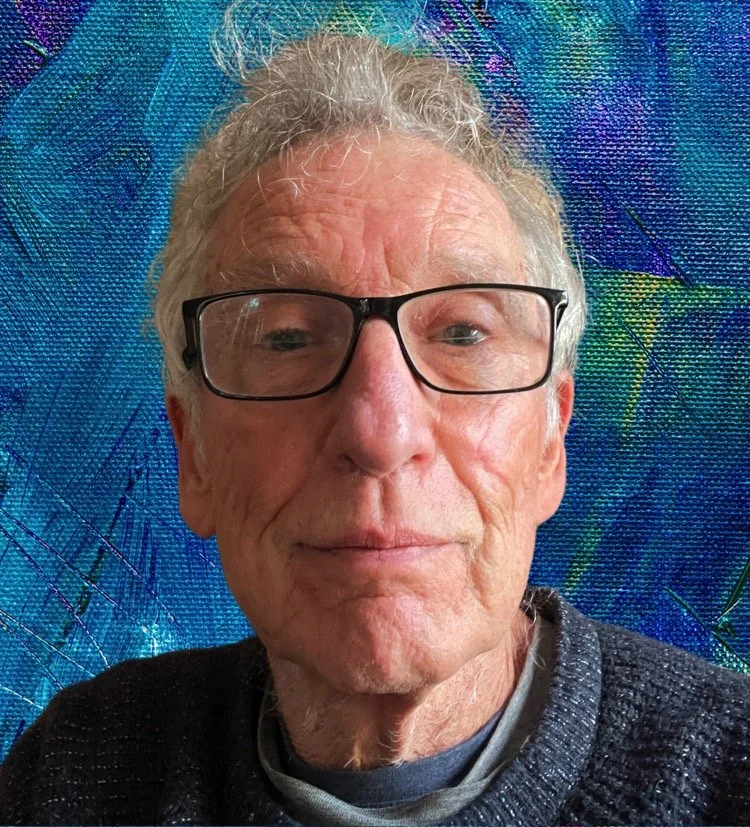 A close-up portrait of an elderly man with glasses, gray hair, and a slight smile, against a colorful, textured background.