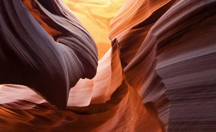 Smooth, colorful, curving sandstone formations in a slot canyon, with layers of orange, red, and purple hues.