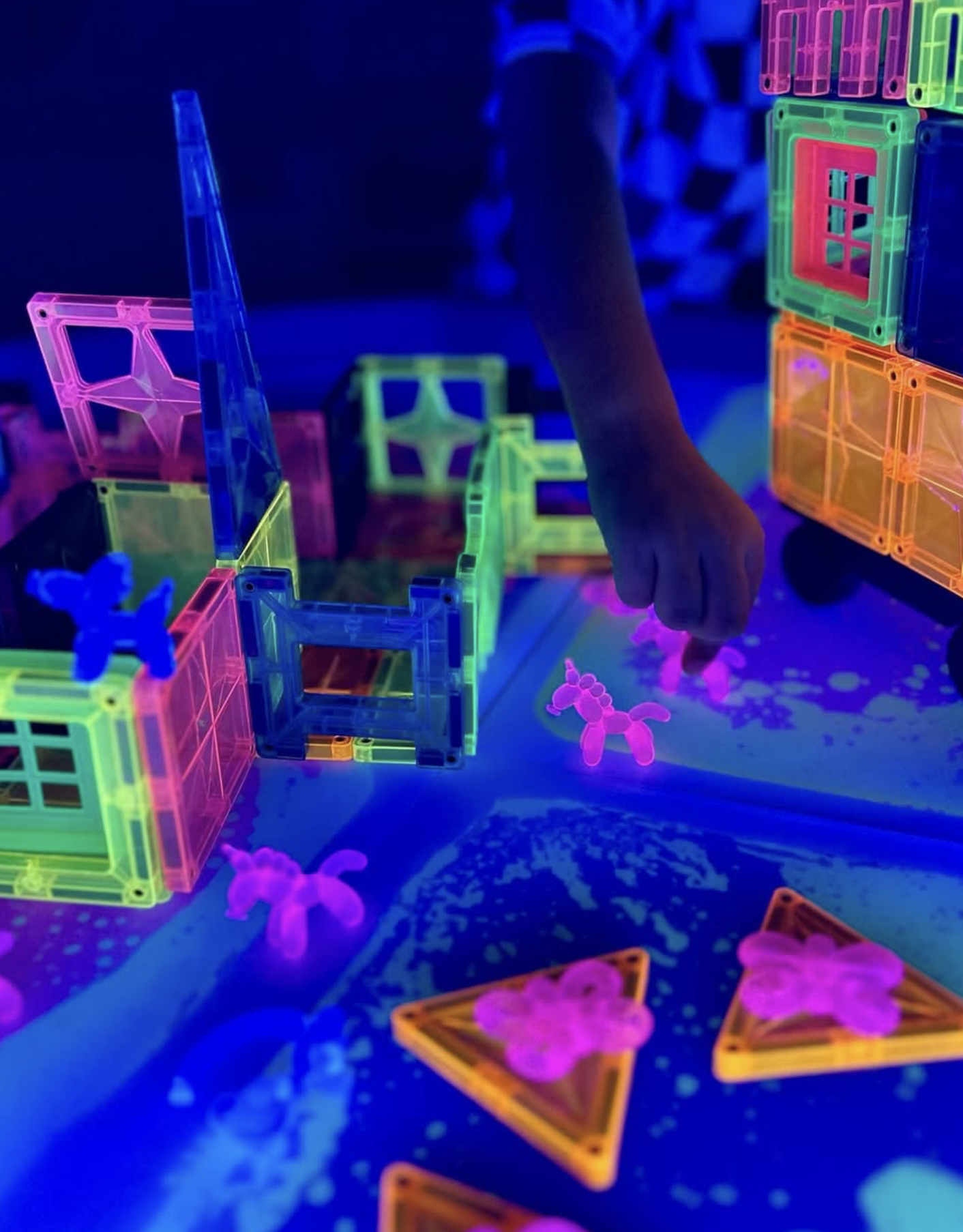 Child playing with glow-in-the-dark magnetic building blocks and animal figurines in the dark.