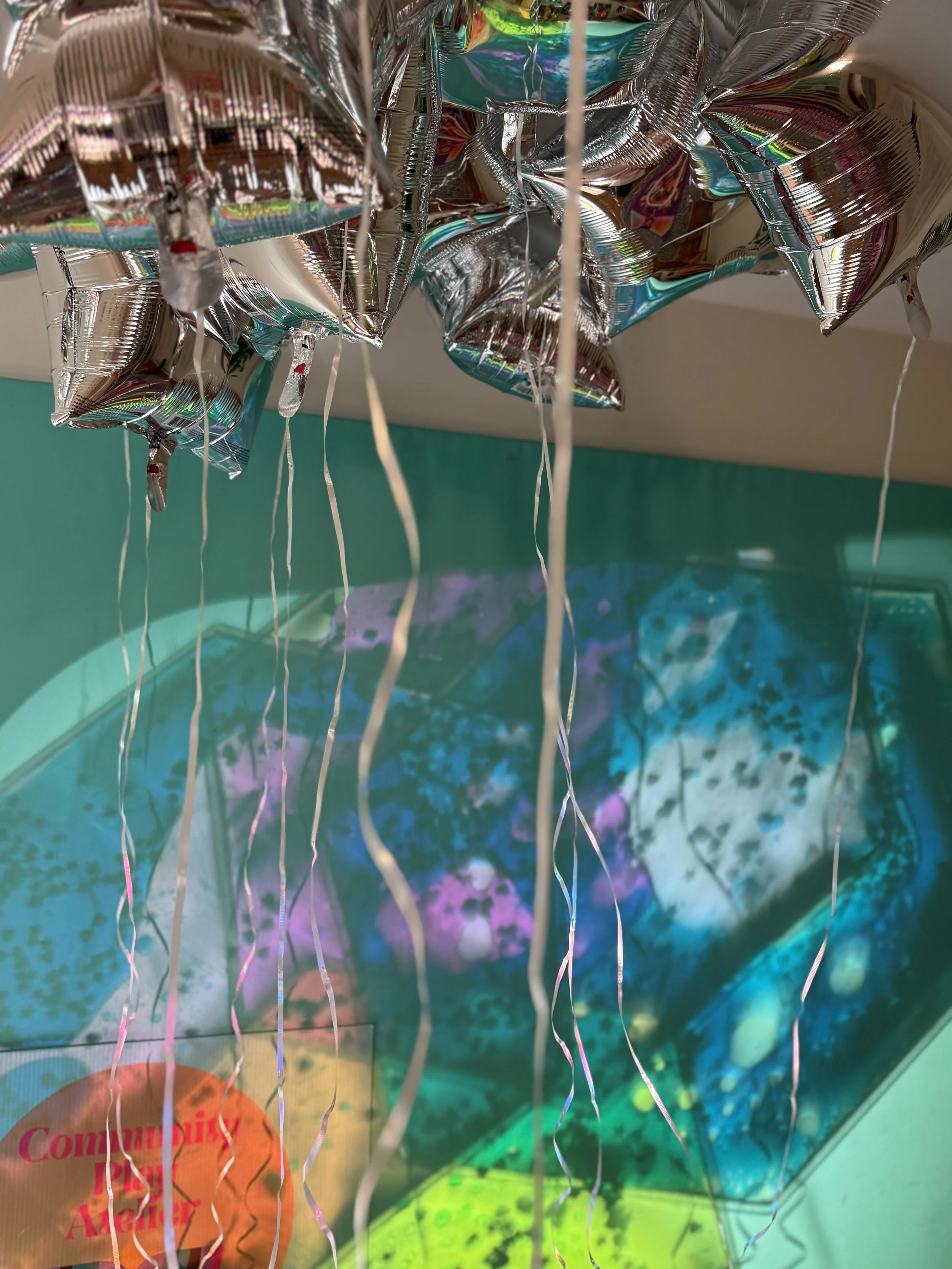 Silver star-shaped balloons with curly ribbons are hanging above an interactive digital display showing a starry sky and planets.