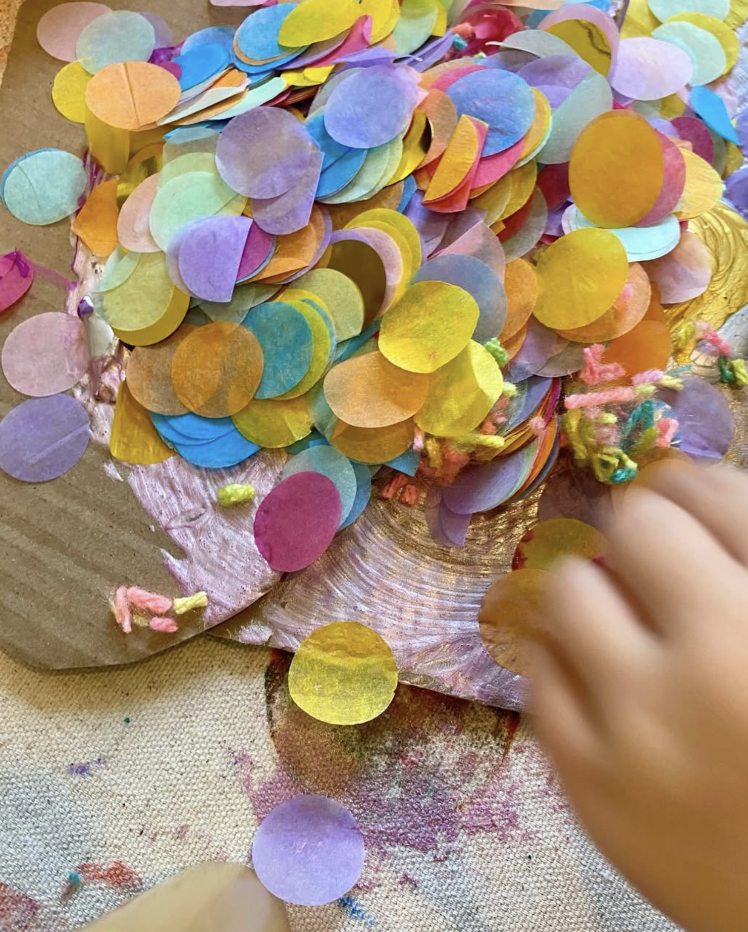 Colorful paper confetti scattered on a textured surface with a child's hand reaching into the pile.