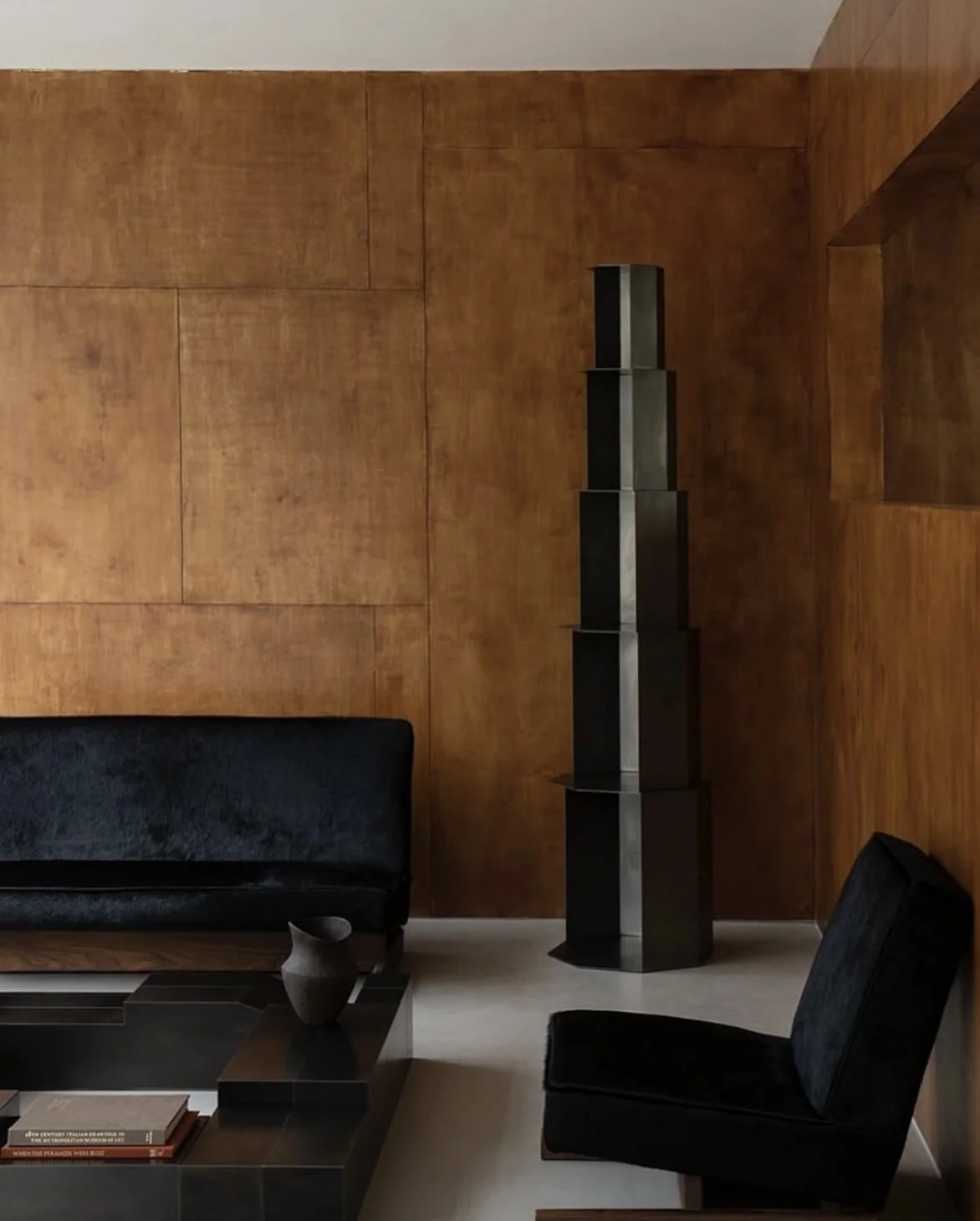 Modern living room with a wooden paneled wall, black sofa, black chair, and a tall black shelving unit.