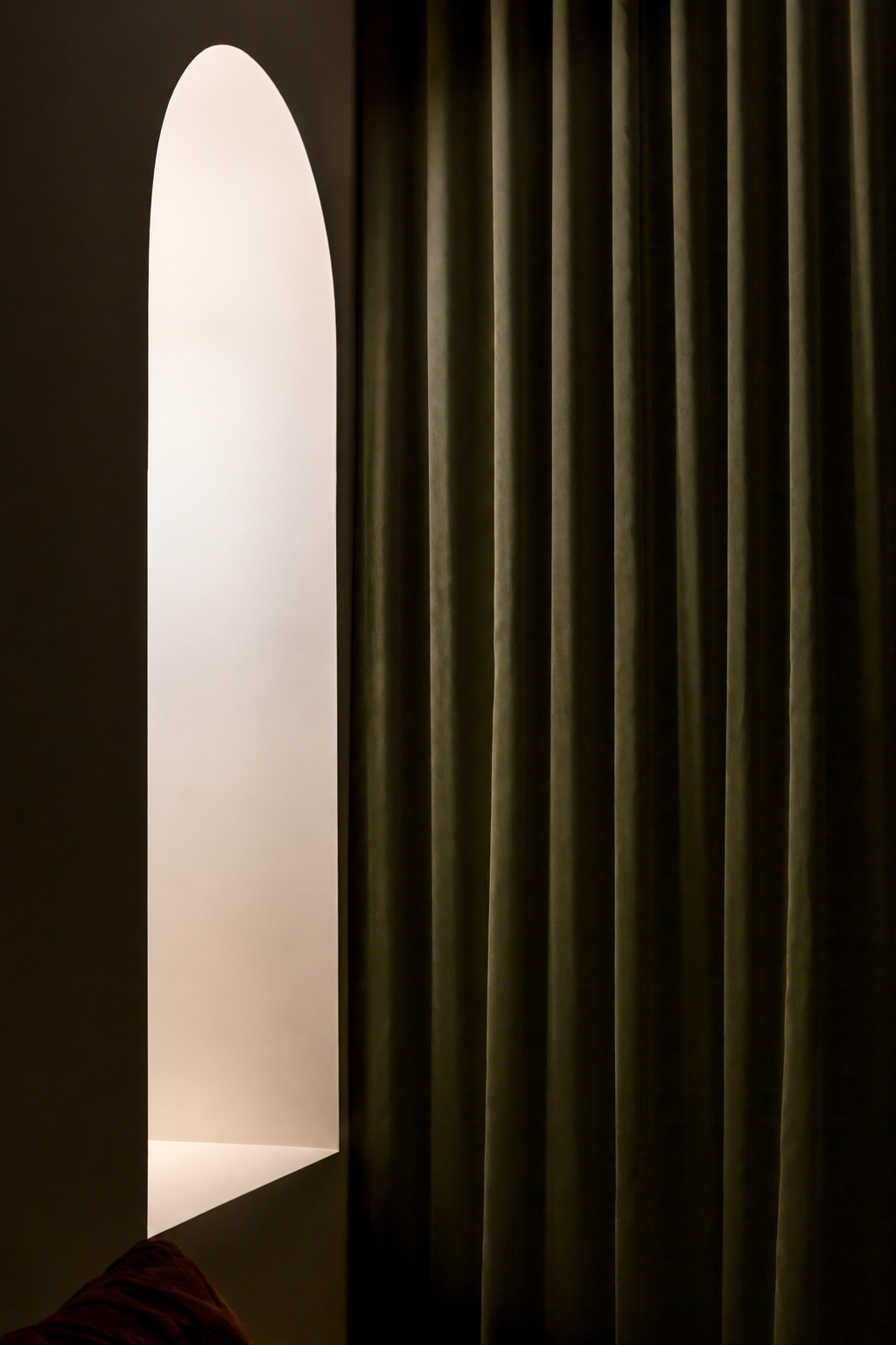 A white arched doorway next to a wall with vertical dark green curtains.