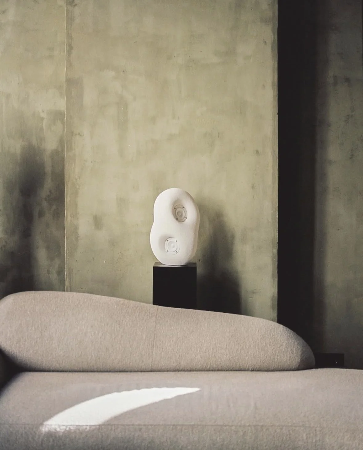 Minimalist living room with a beige couch, a textured wall, and a modern white sculpture on a pedestal in the background.
