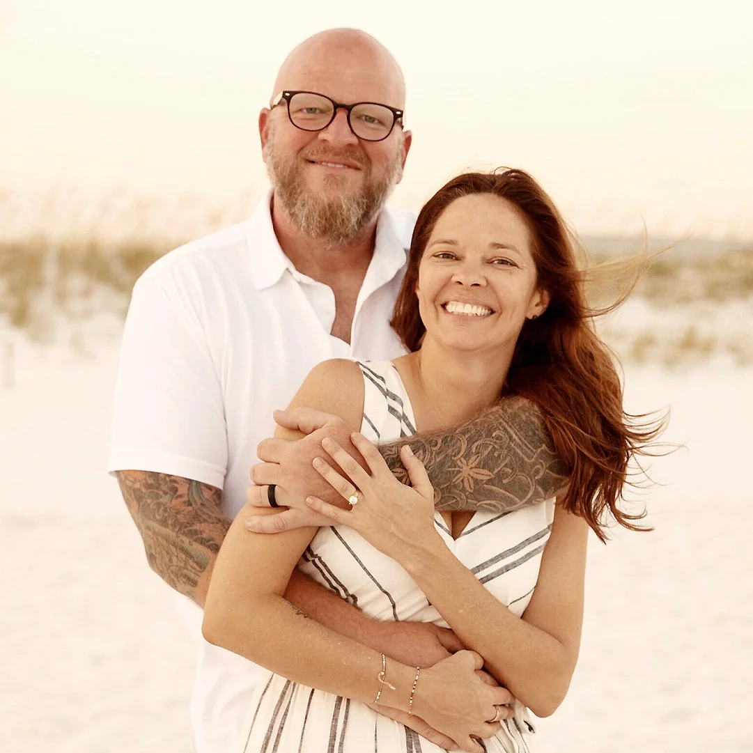 Smiling couple embracing on a bright beach, with warm sunlight and ocean in the background