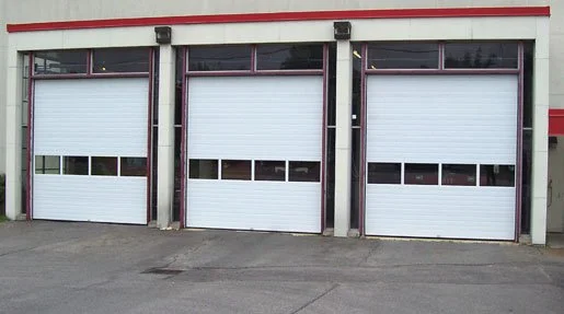 Three white garage doors with horizontal windows, on a building with a concrete driveway.