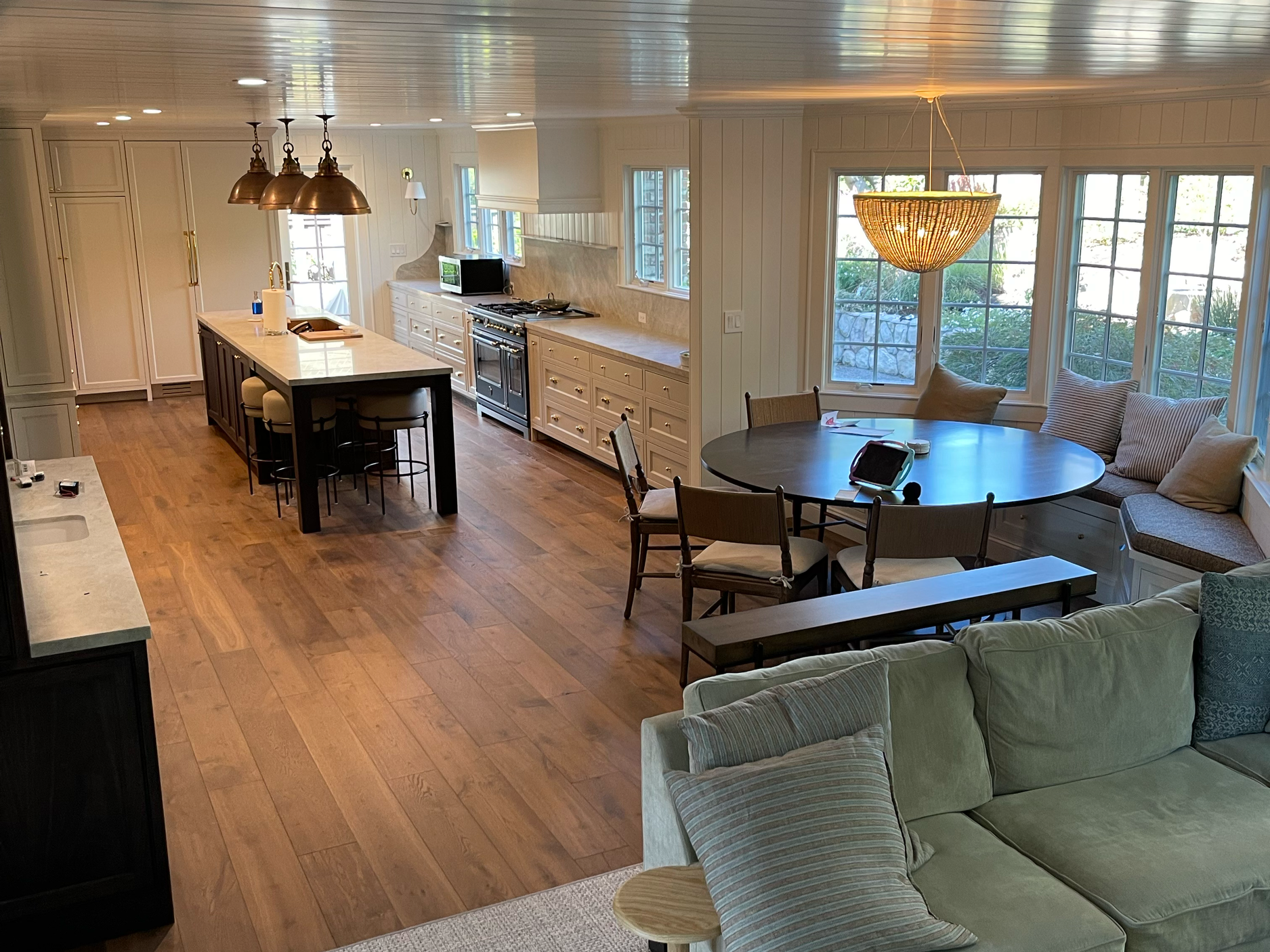 Open-concept living room and kitchen with hardwood floors, a large island, and a round dining nook near windows.