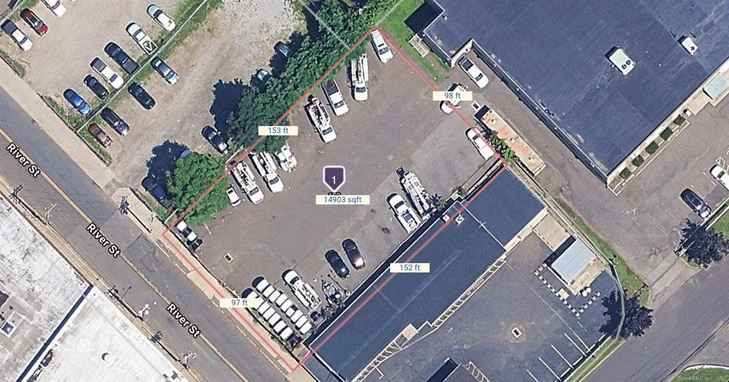 Aerial view of a parking lot surrounded by buildings, with cars parked in spaces and a sidewalk along River Street.