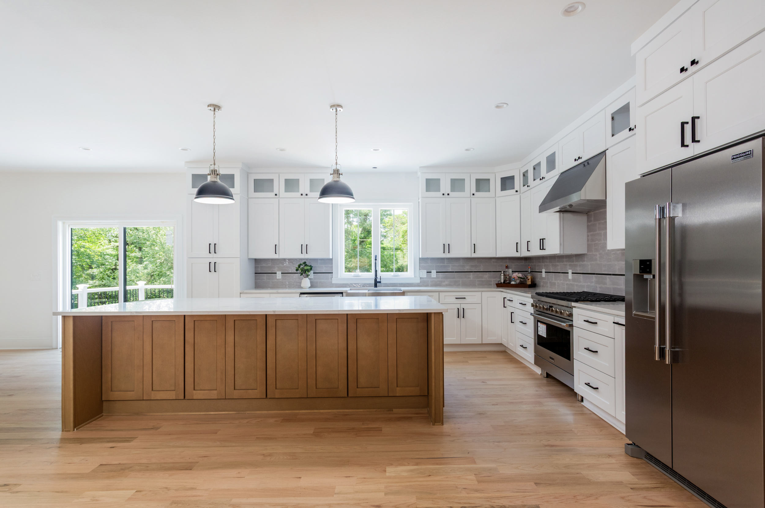 Modern kitchen with white cabinets, stainless steel appliances, a wooden island, and a window showing green trees outside.