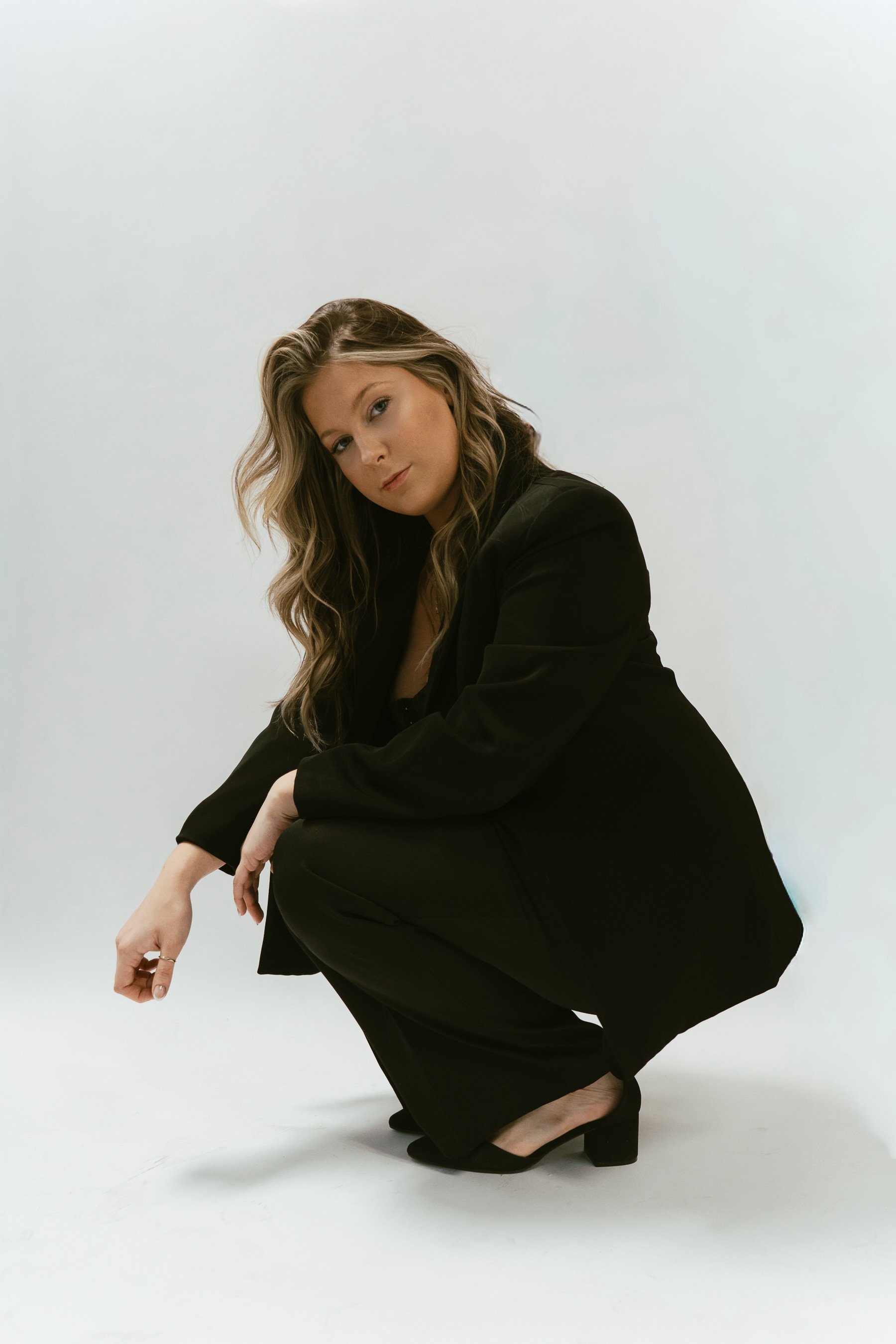 Woman wearing a black suit squatting against a plain white background.