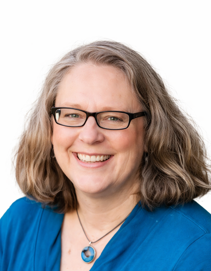 A smiling woman with shoulder-length wavy hair, wearing glasses, a blue shirt, and a pendant necklace, posed against a plain white background.