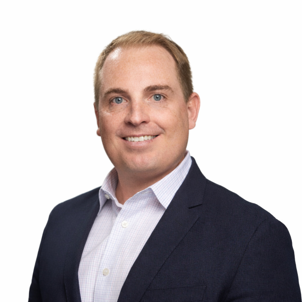 Portrait of a man with short light brown hair, blue eyes, wearing a dark blazer and white dress shirt, smiling against a white background.