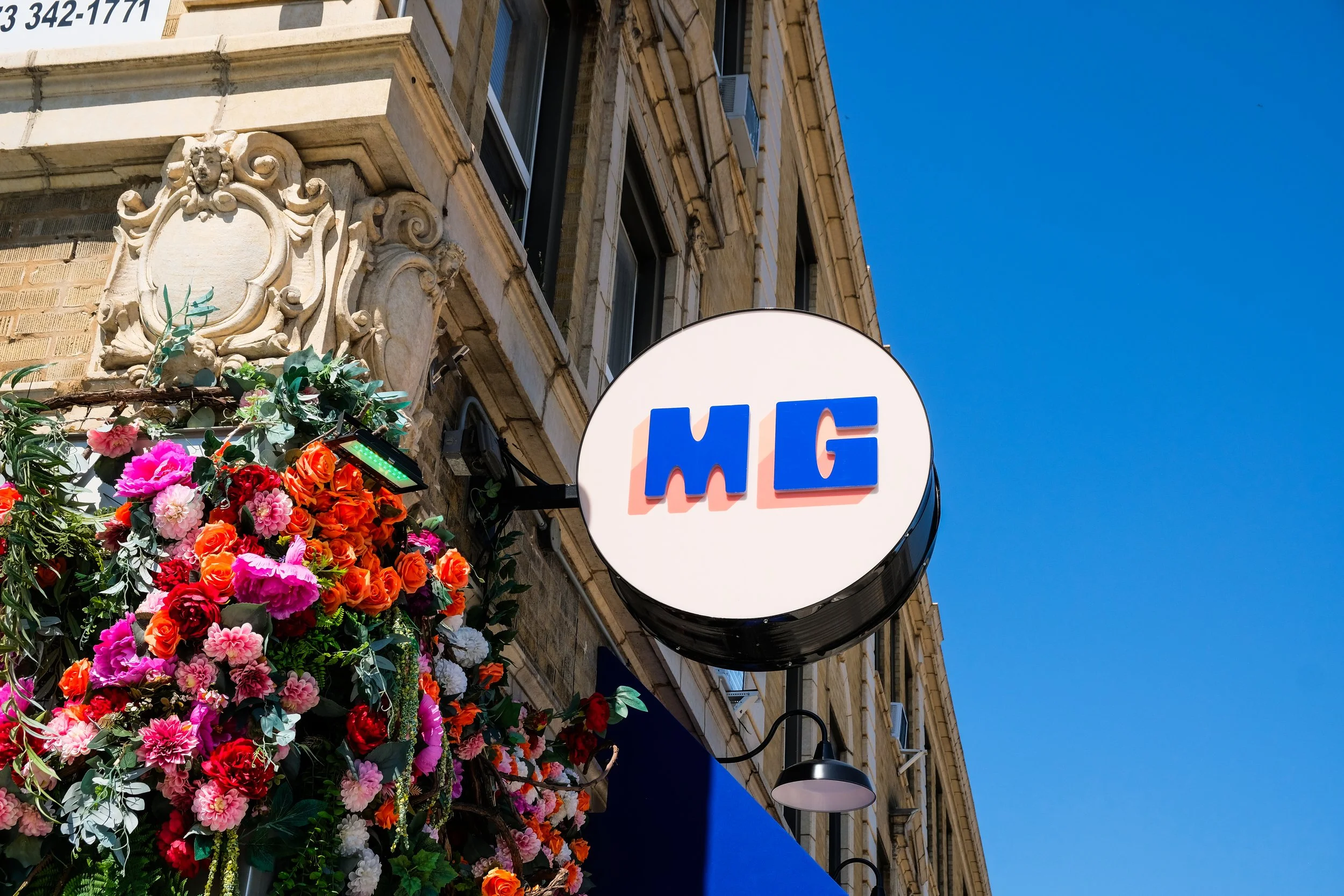 Circular blade sign for the restaurant Mucho Gusto featuring its initials MG