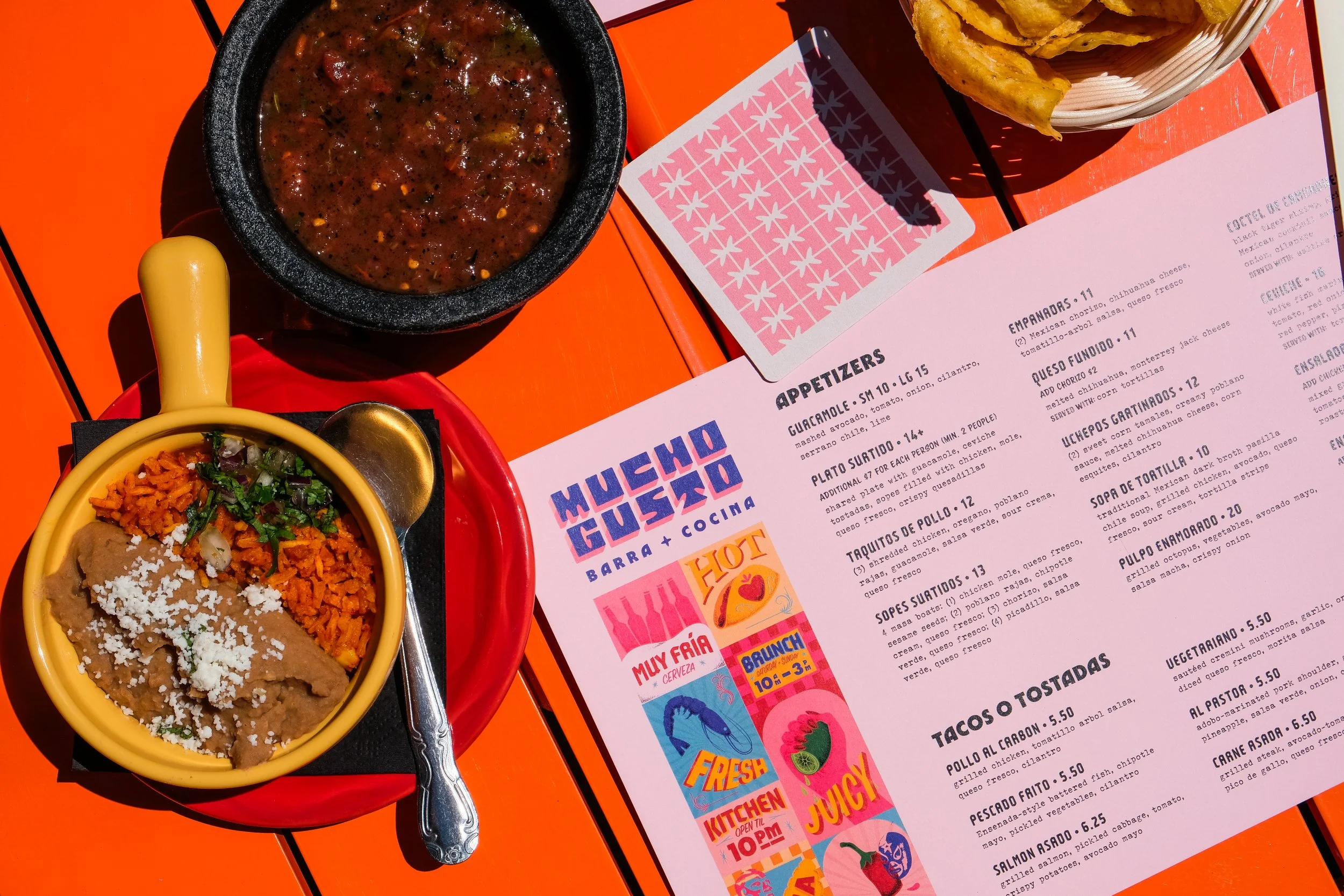 Colorful and illustrated menus for the restaurant Mucho Gusto sit atop an orange table