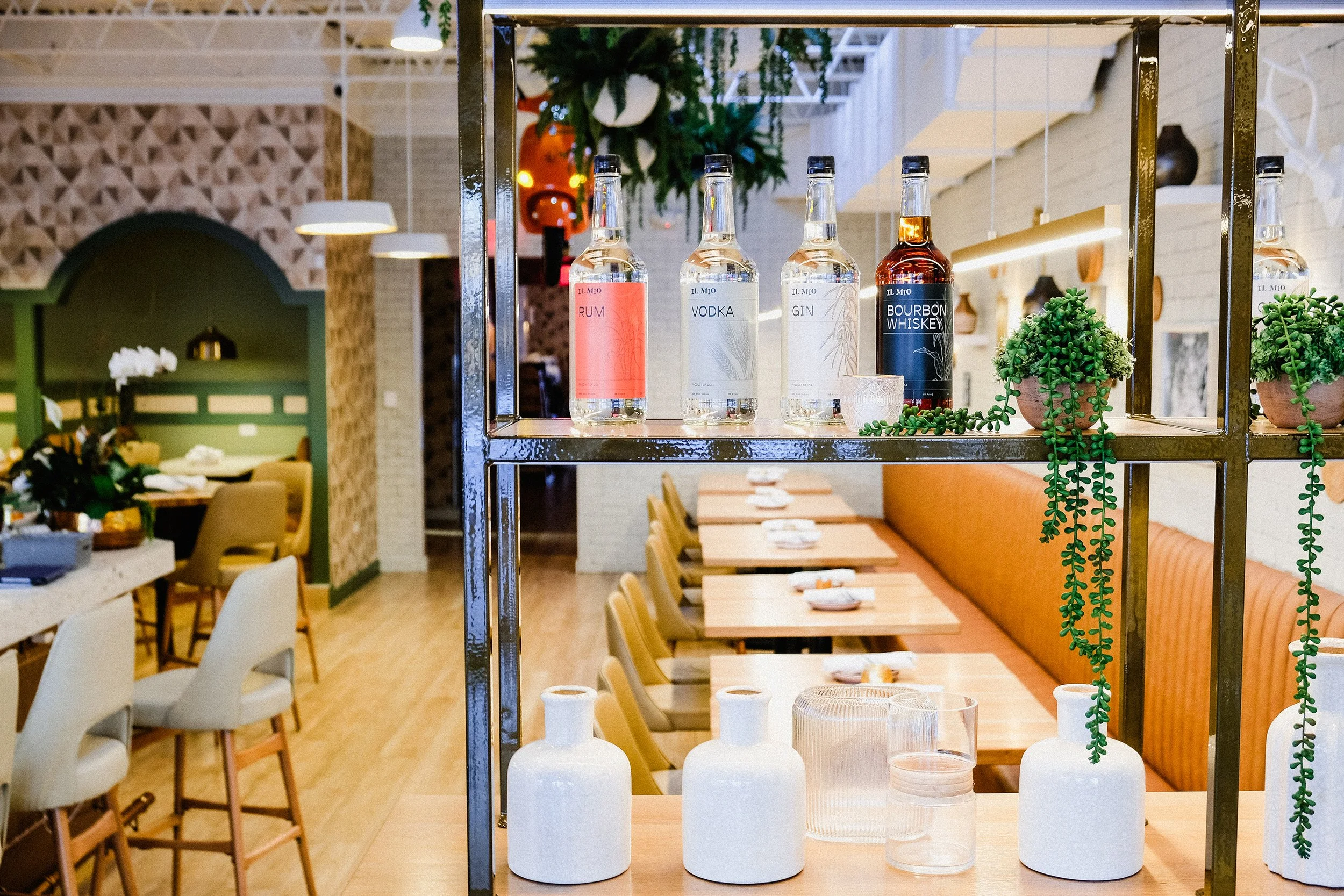 Branded alcohol bottles sit on a metal framed shelf within Il Mio, a cozy Italian restaurant