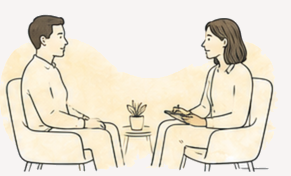 A man and woman seated across from each other in chairs, having a conversation in a therapy or counseling session, with a small plant on a table between them.