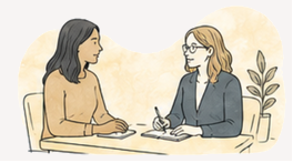 Two women having a discussion at a desk in an office setting, one is taking notes.