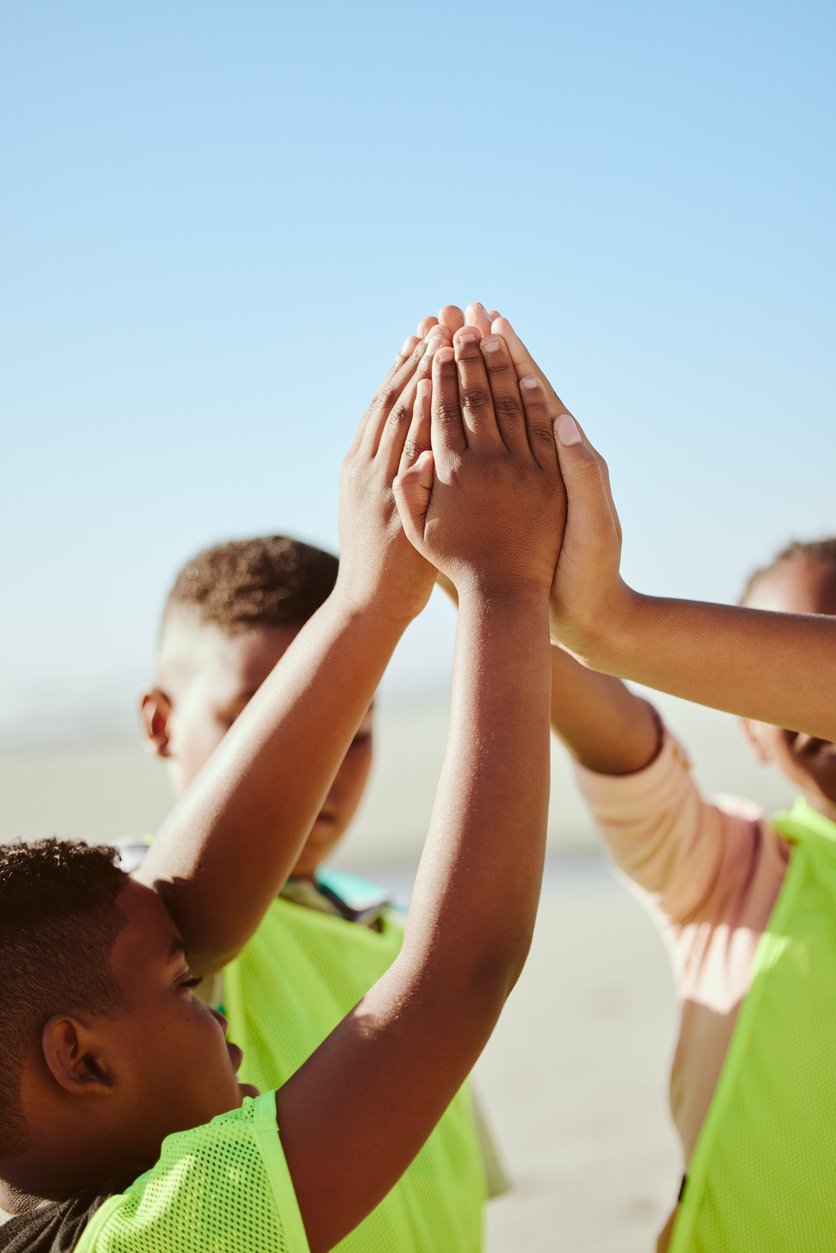 Group of children giving high five together outdoors on a sunny day.
