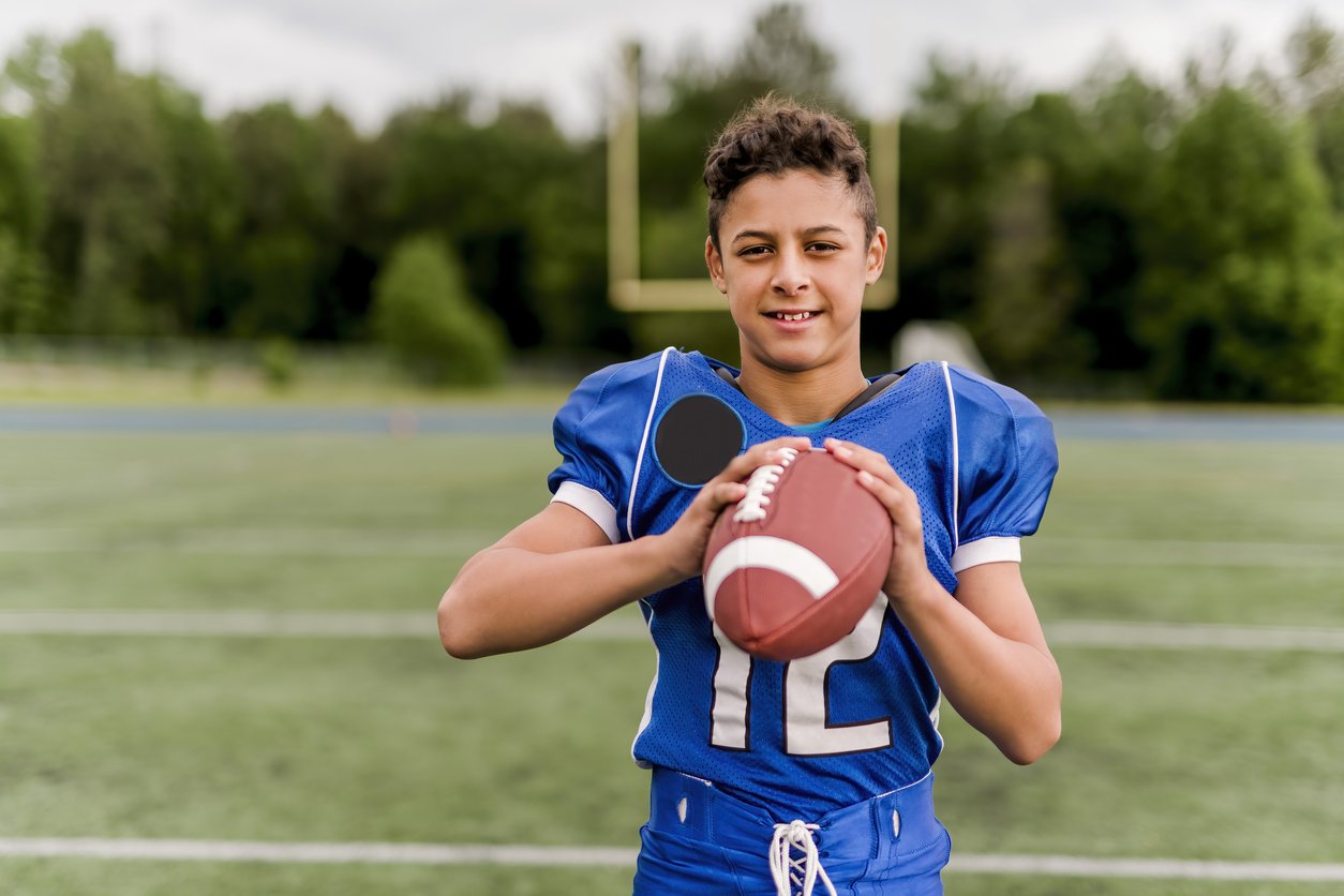Young boy holding a football in a football uniform