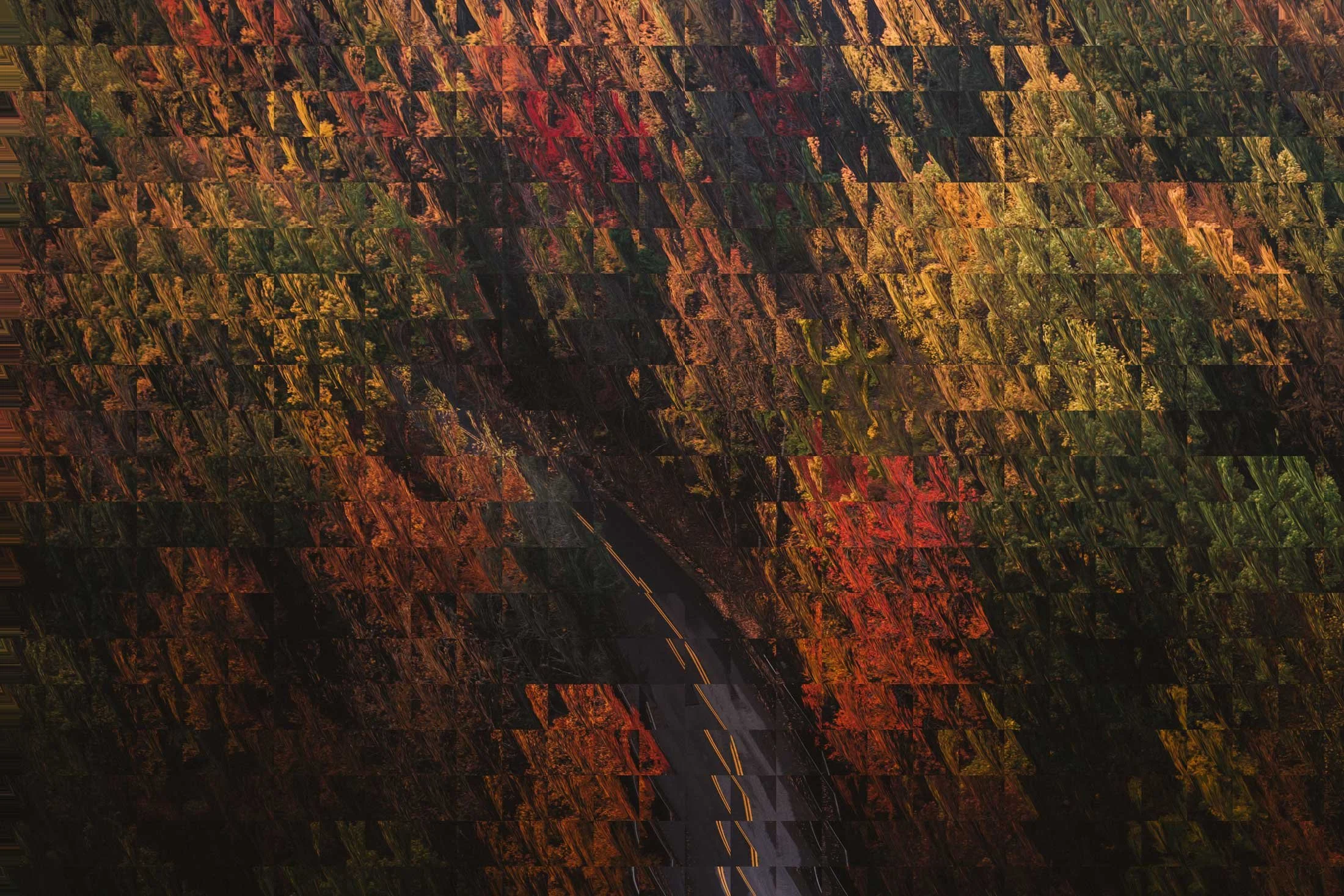 A winding road surrounded by vibrant fall foliage with trees in red, orange, yellow, and green, seen through a geometric, mosaic-like filter effect.