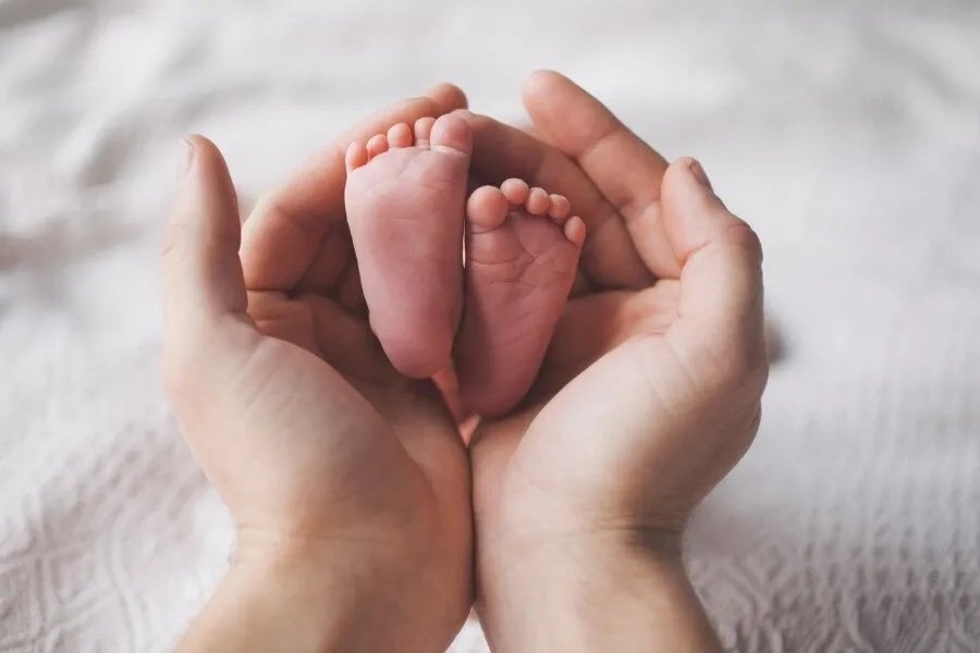 A pair of adult hands gently holding a tiny newborn baby's feet.