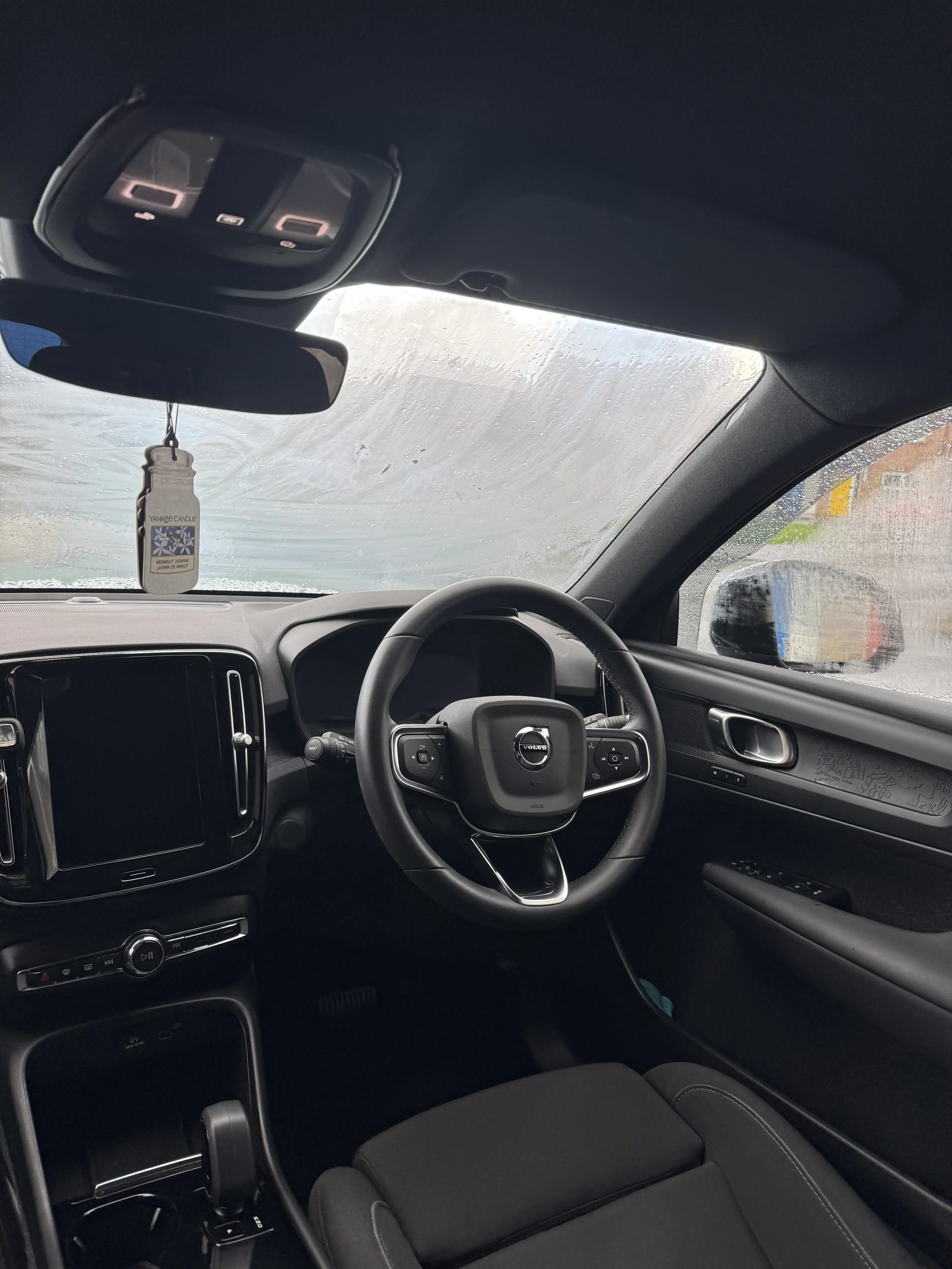 Interior of a Volvo car with a rain-covered windshield, steering wheel, and dashboard.