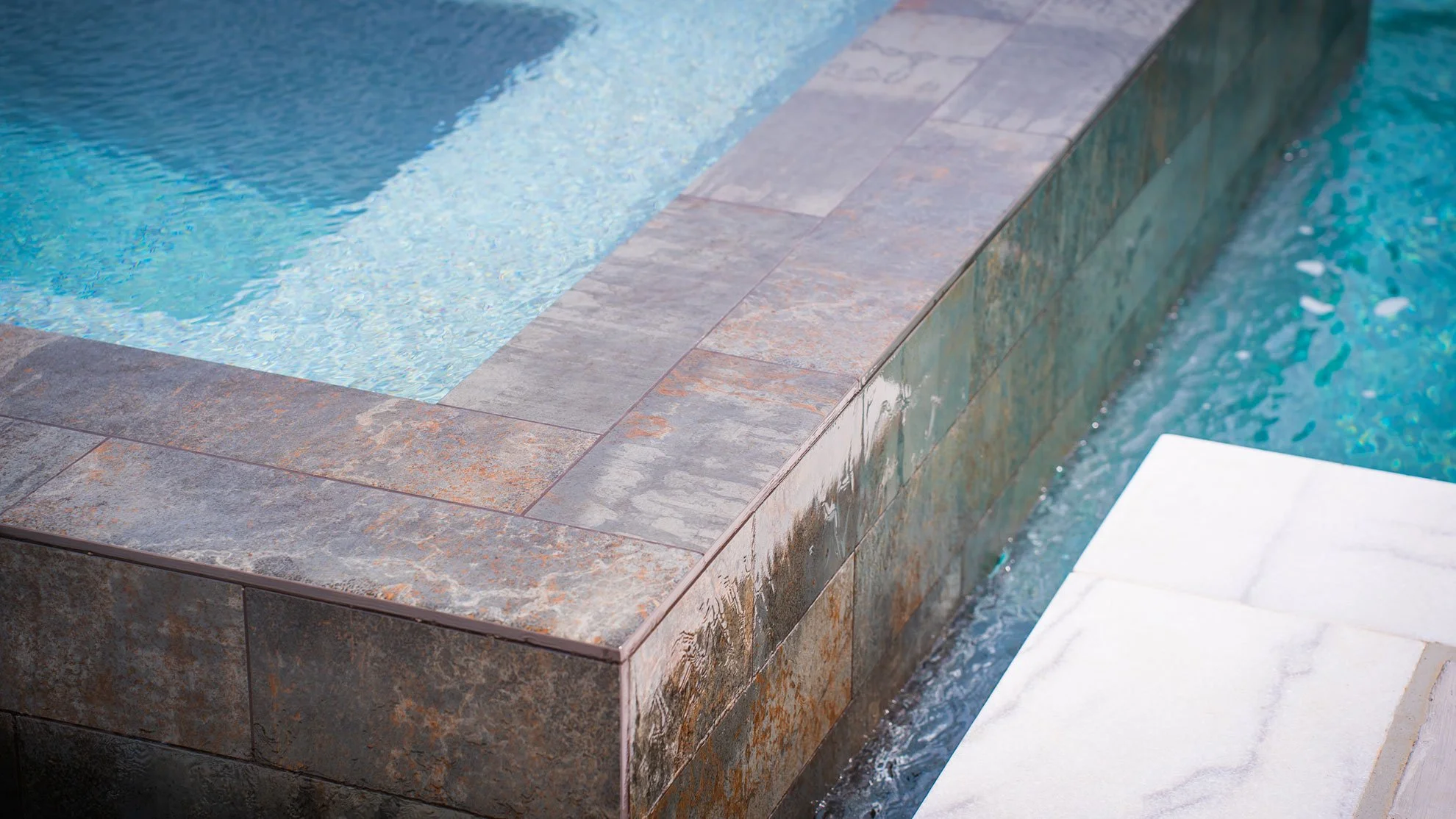Close-up of an outdoor swimming pool corner with stone tiles and a white pool step.