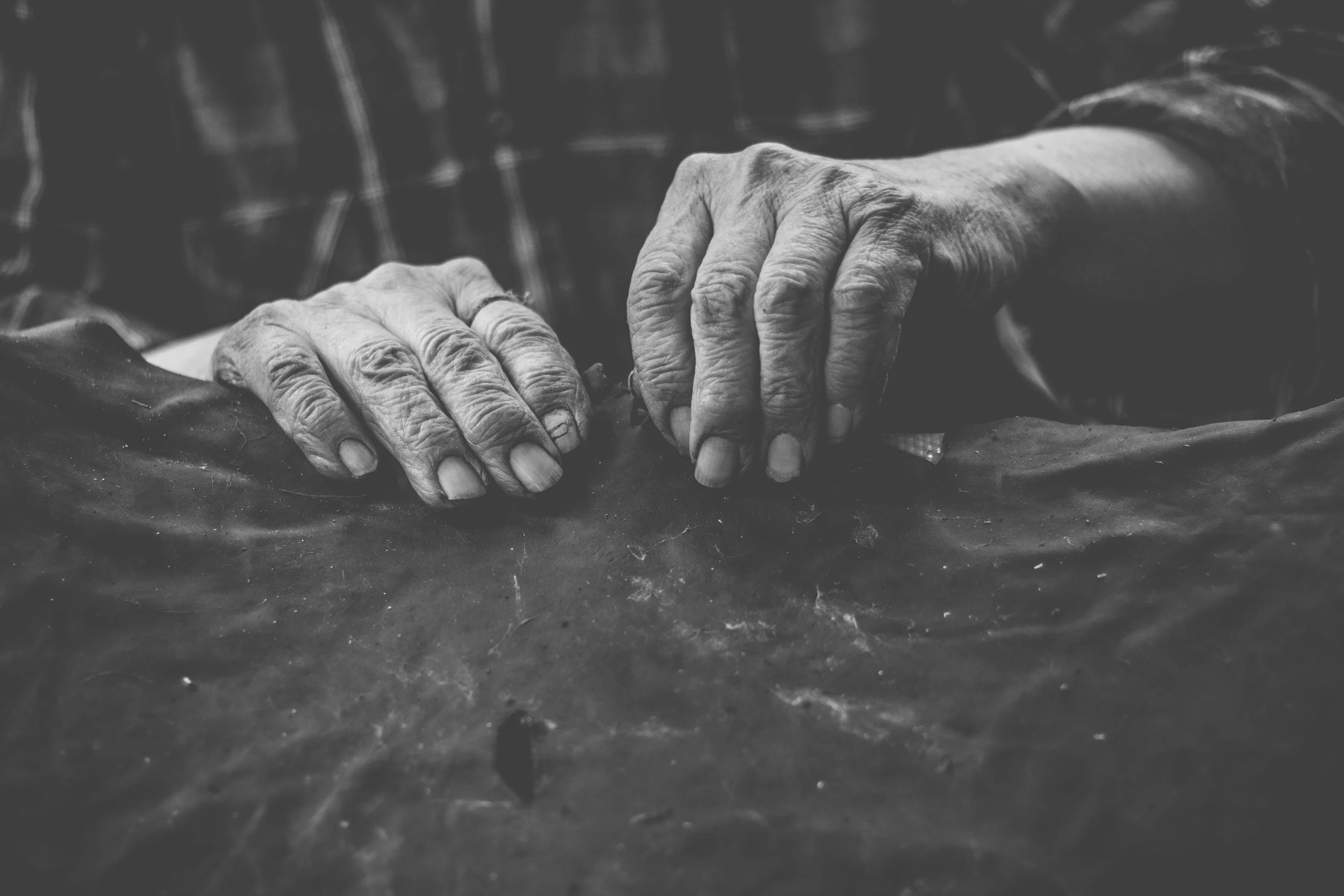 Close-up of elderly person's hands resting on a table, gripping a piece of fabric, in black and white.