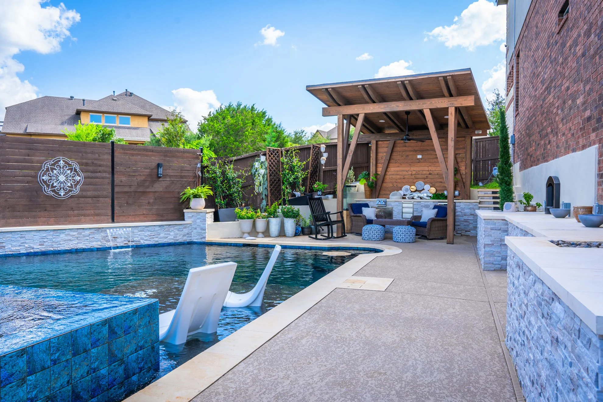 Backyard with swimming pool, outdoor seating, and a covered patio area with plants and decorative elements.