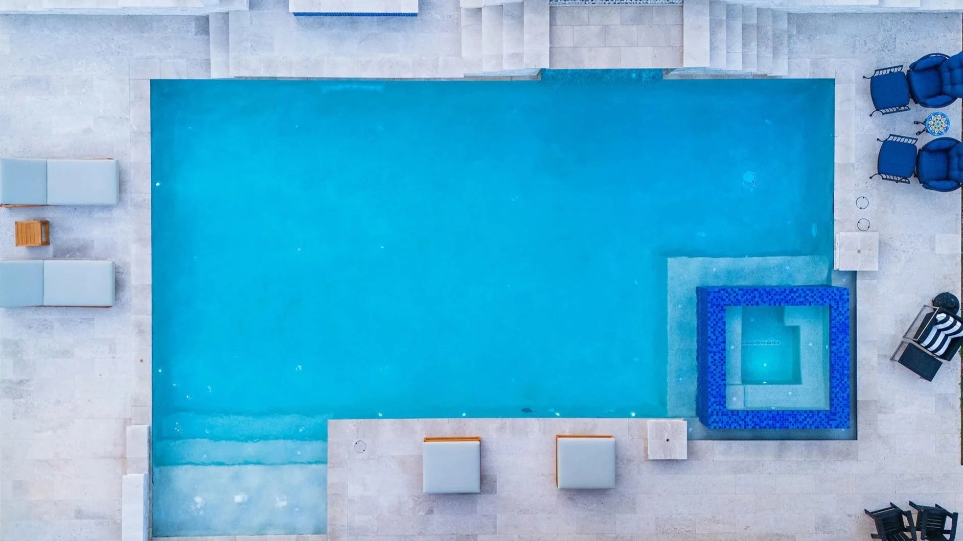 Top-down view of a swimming pool with stairs, lounge chairs, and seating area around it.