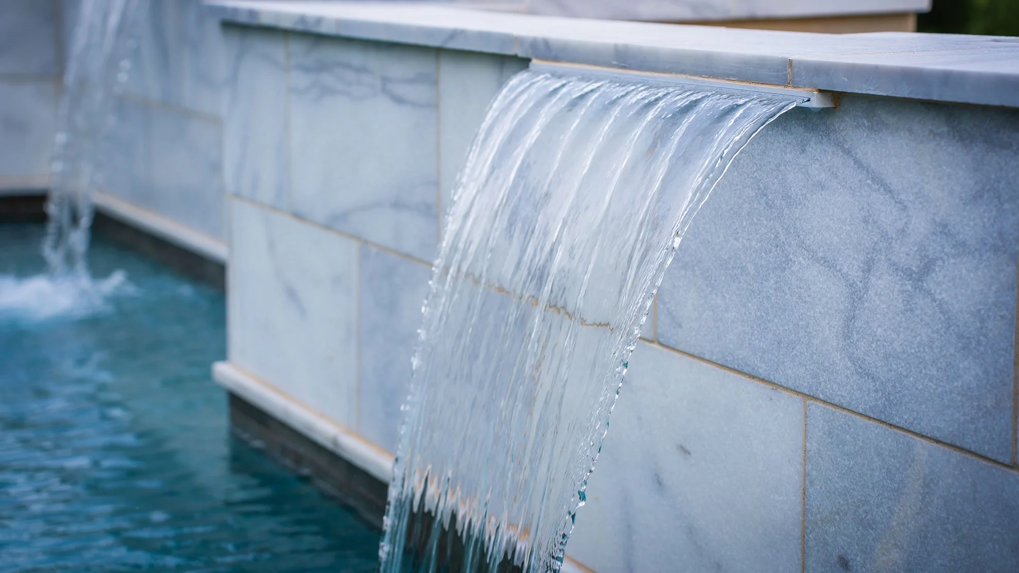 Water flowing over a gray stone fountain edge into a pool.