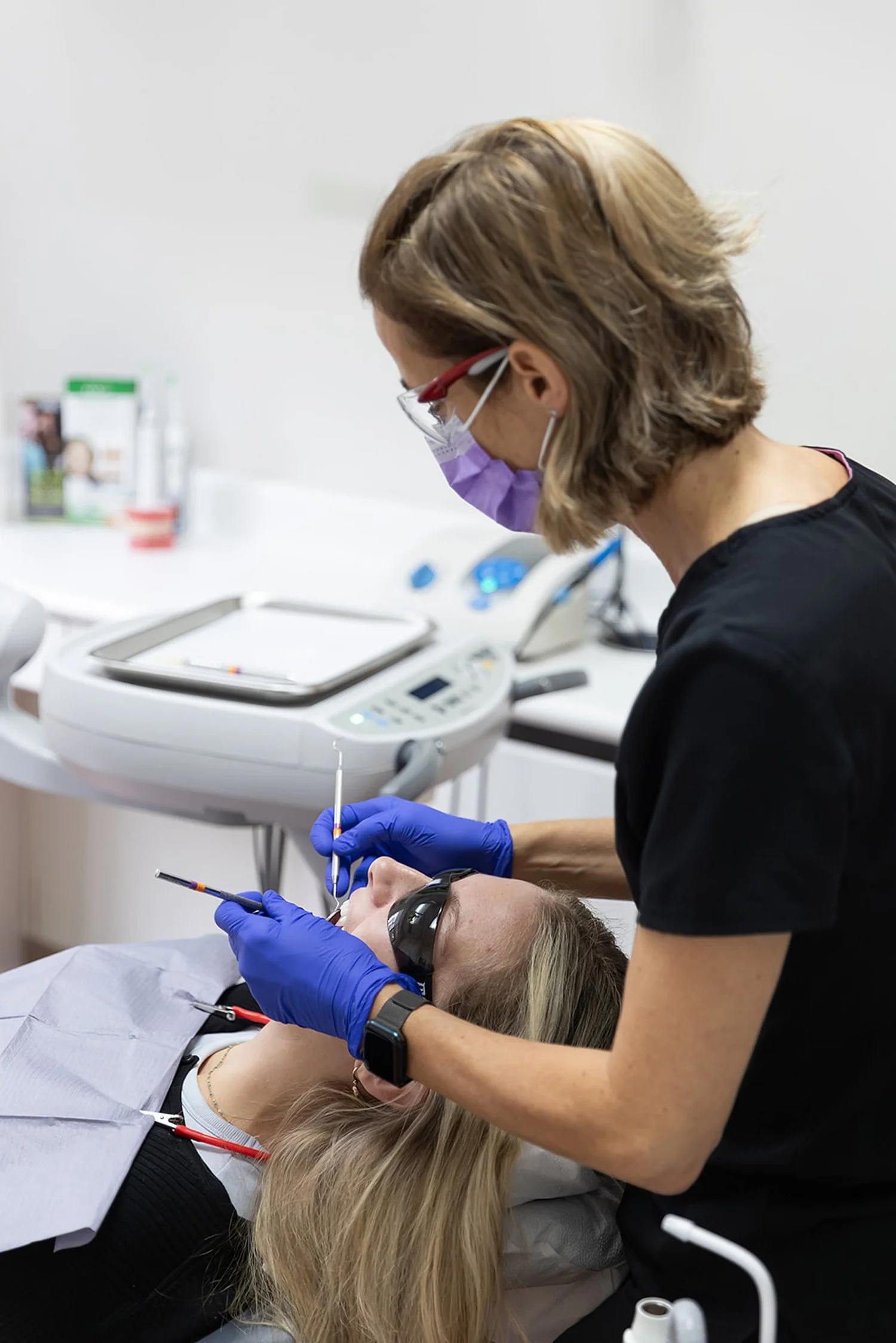 Dentist or dental technician performing a dental procedure on a patient lying in a dental chair in a clinical setting.
