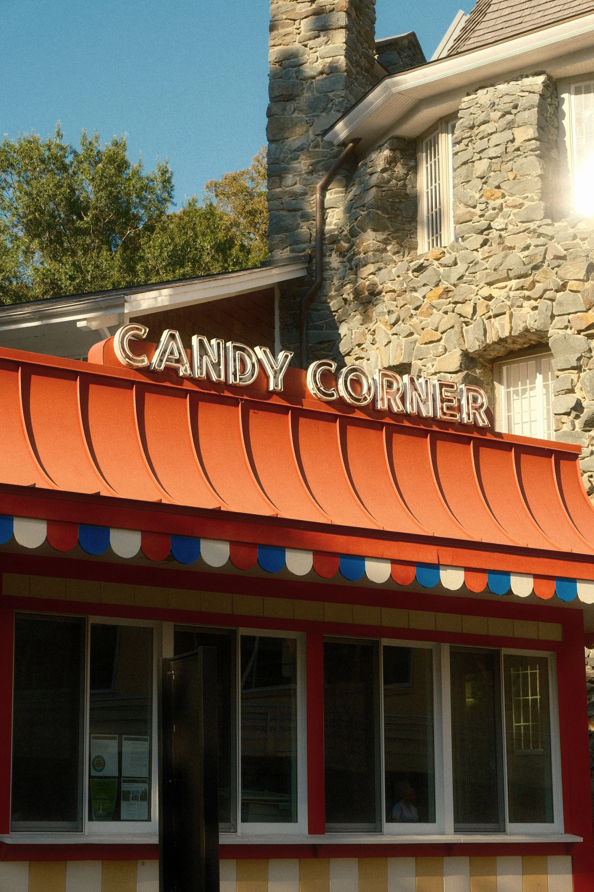 Candy Corner storefront with red and orange striped awning, sign reading 'CANDY CORNER', and stone building in the background.