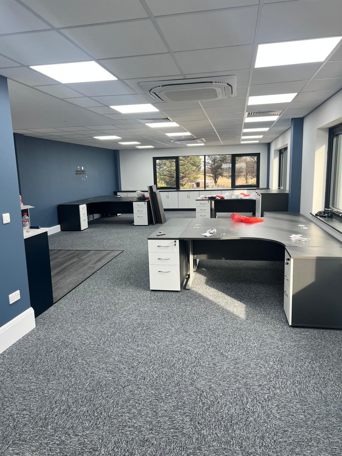 Empty office space with multiple desks and windows, under renovation or setup.