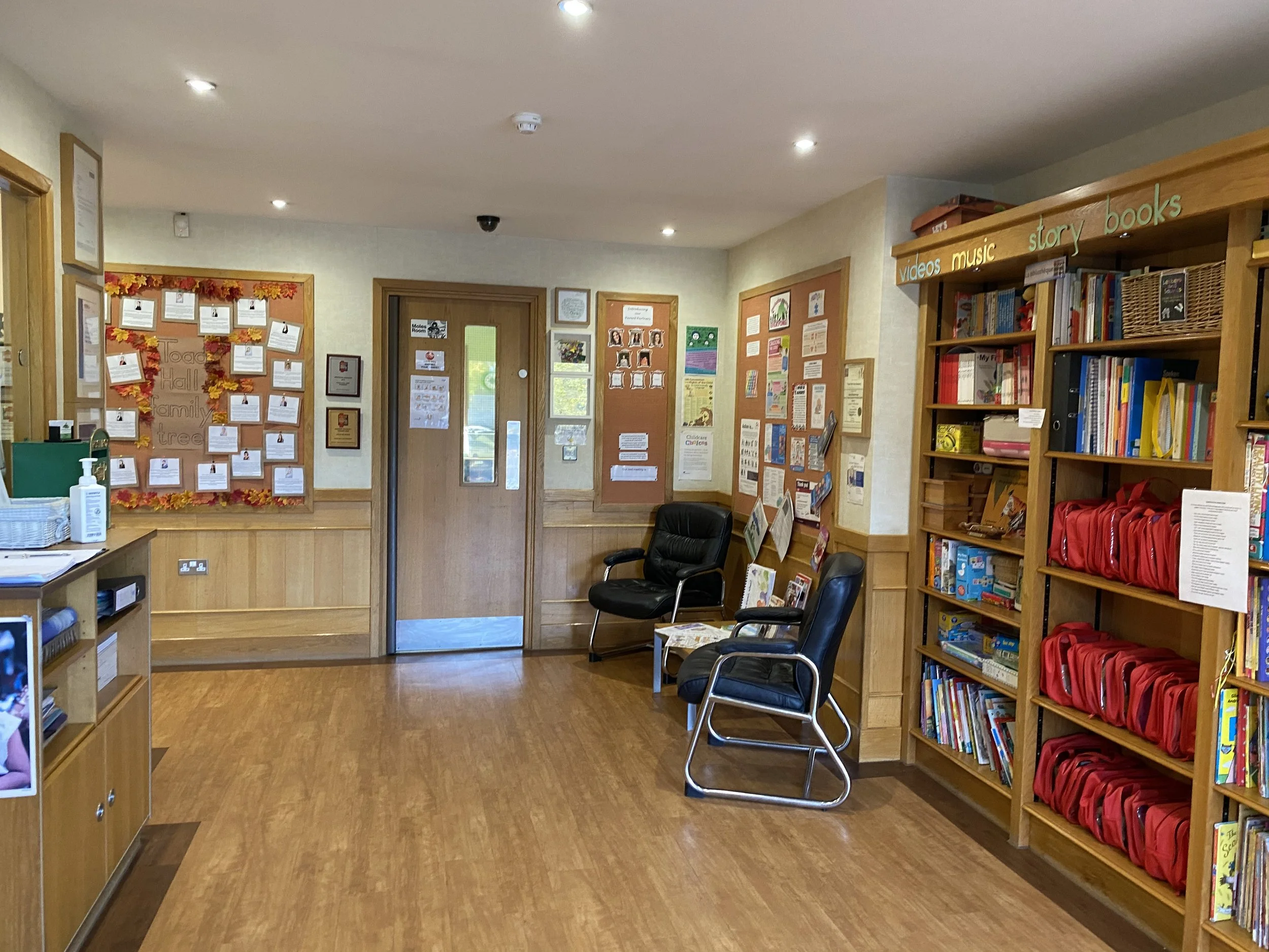 Inside a library or classroom with bookshelves, armchairs, and bulletin boards decorated with papers and artwork.