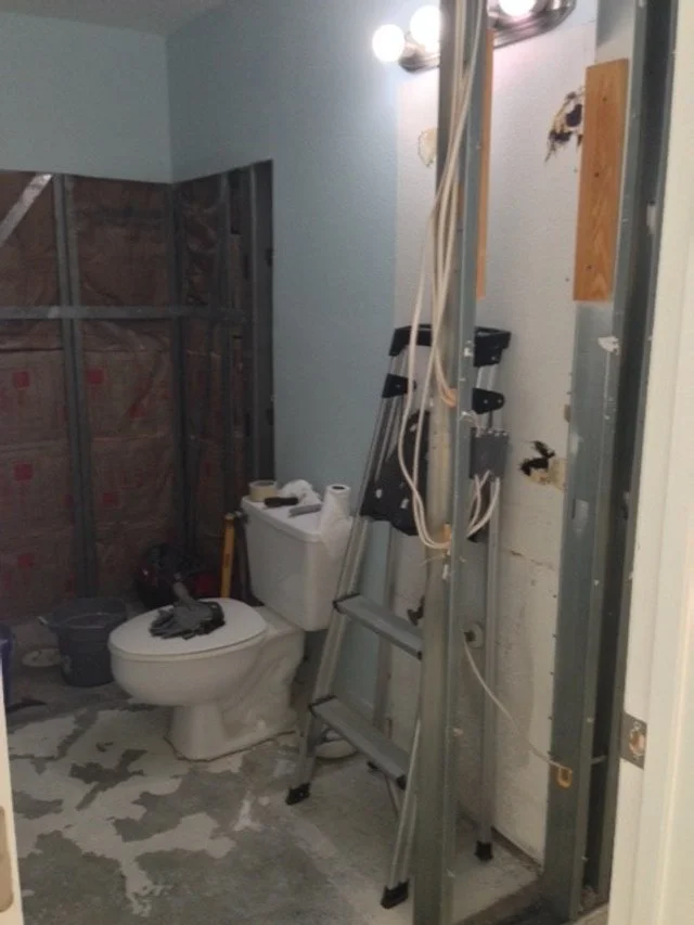 Bathroom renovation in progress with exposed wall studs, a toilet, ladder, and construction tools.