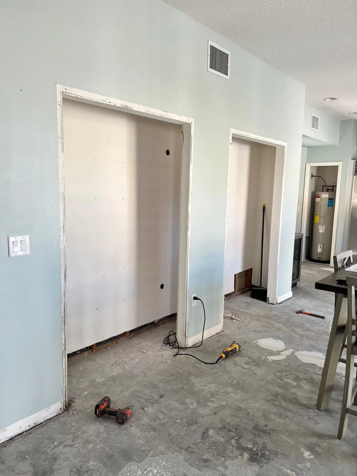 Interior room under renovation with two doorways, construction tools on the unfinished floor, and a water heater in the background.