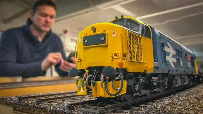 Simon George  can be seen here modelling in action, on his Heaton Lodge Junction, known as Britain's Biggest Model Railway.  It really is realism redefined.   Simon George's yellow and blue British locomotive on a miniature railway track.