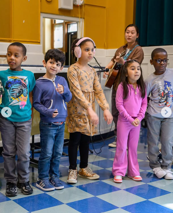 A teacher and young students gather in the gym
