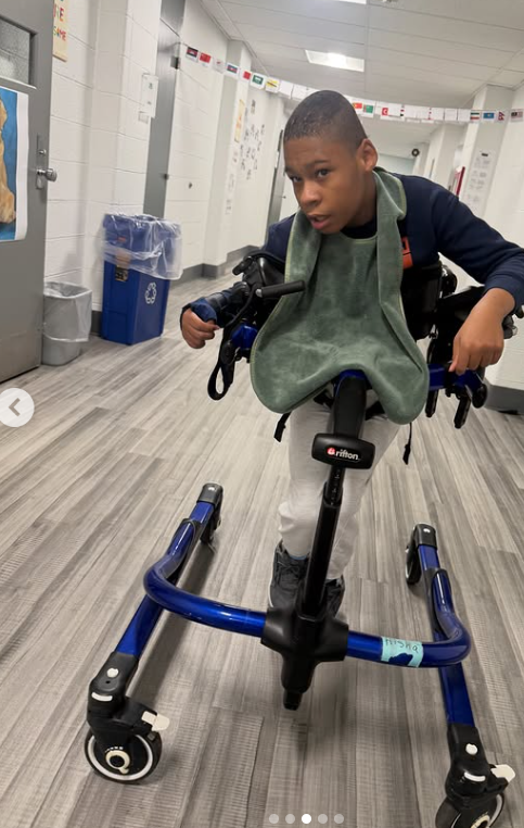 A student practices walking in a gait trainer with his physical therapist