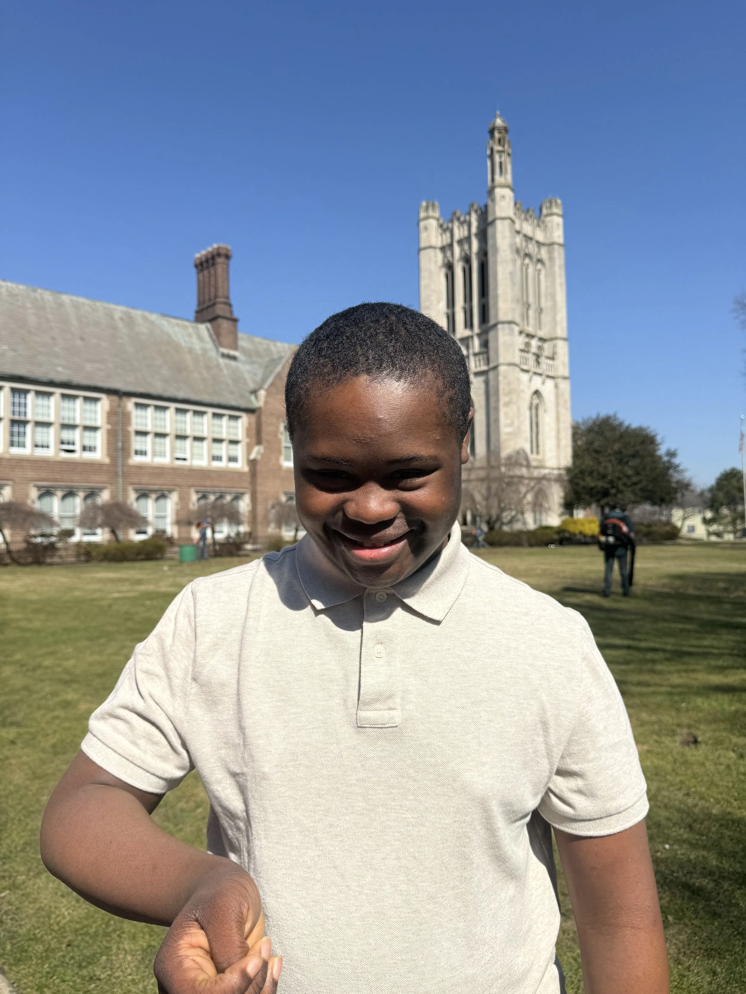 A student smiles on campus with the Kean Jersey City tower behind him