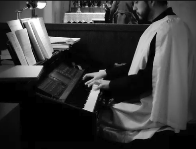 A person dressed in a gown playing the piano in a room with books and a window.