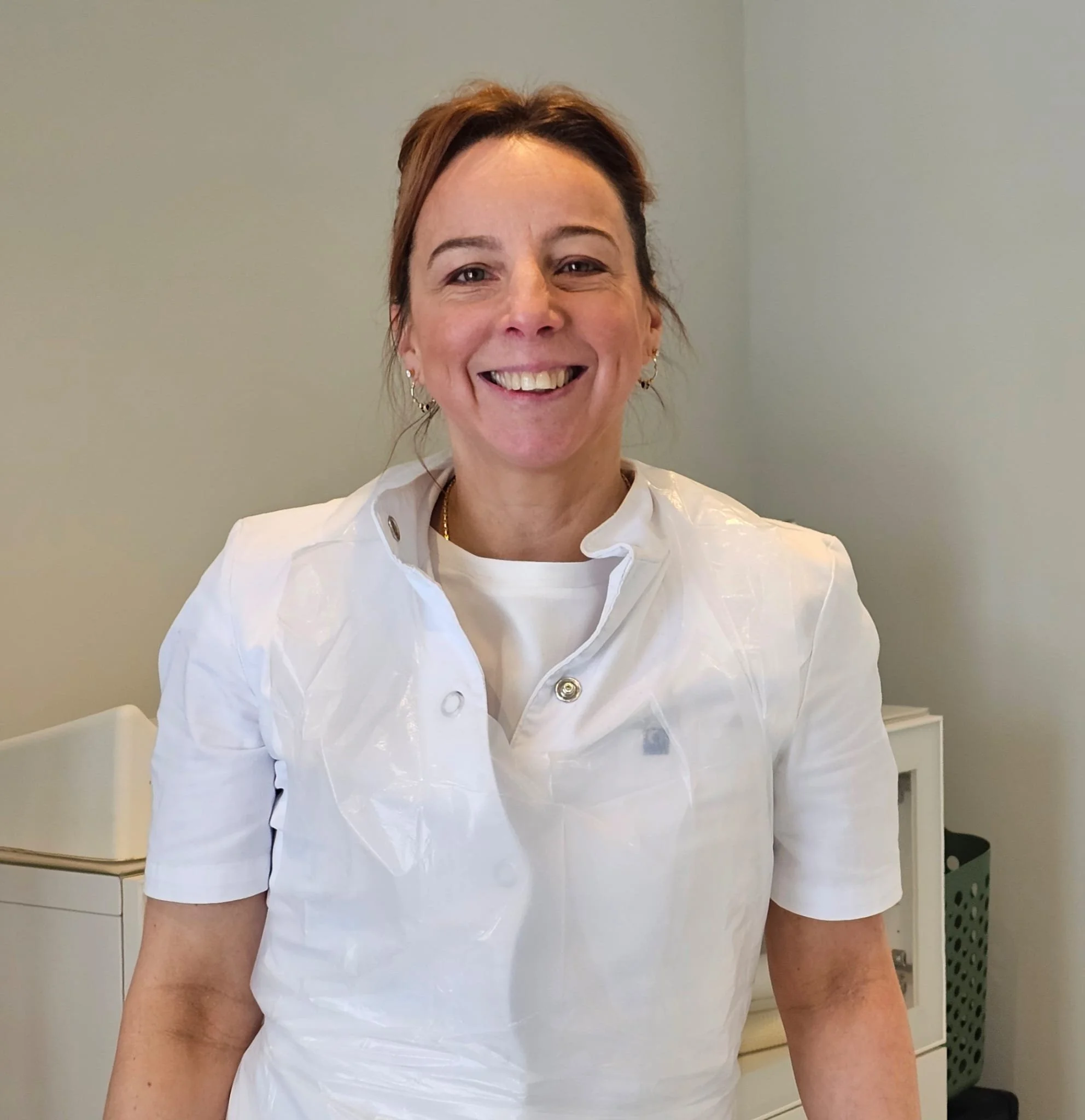 Vrouw in een wit uniform glimlacht in een klinische of laboratorium setting.