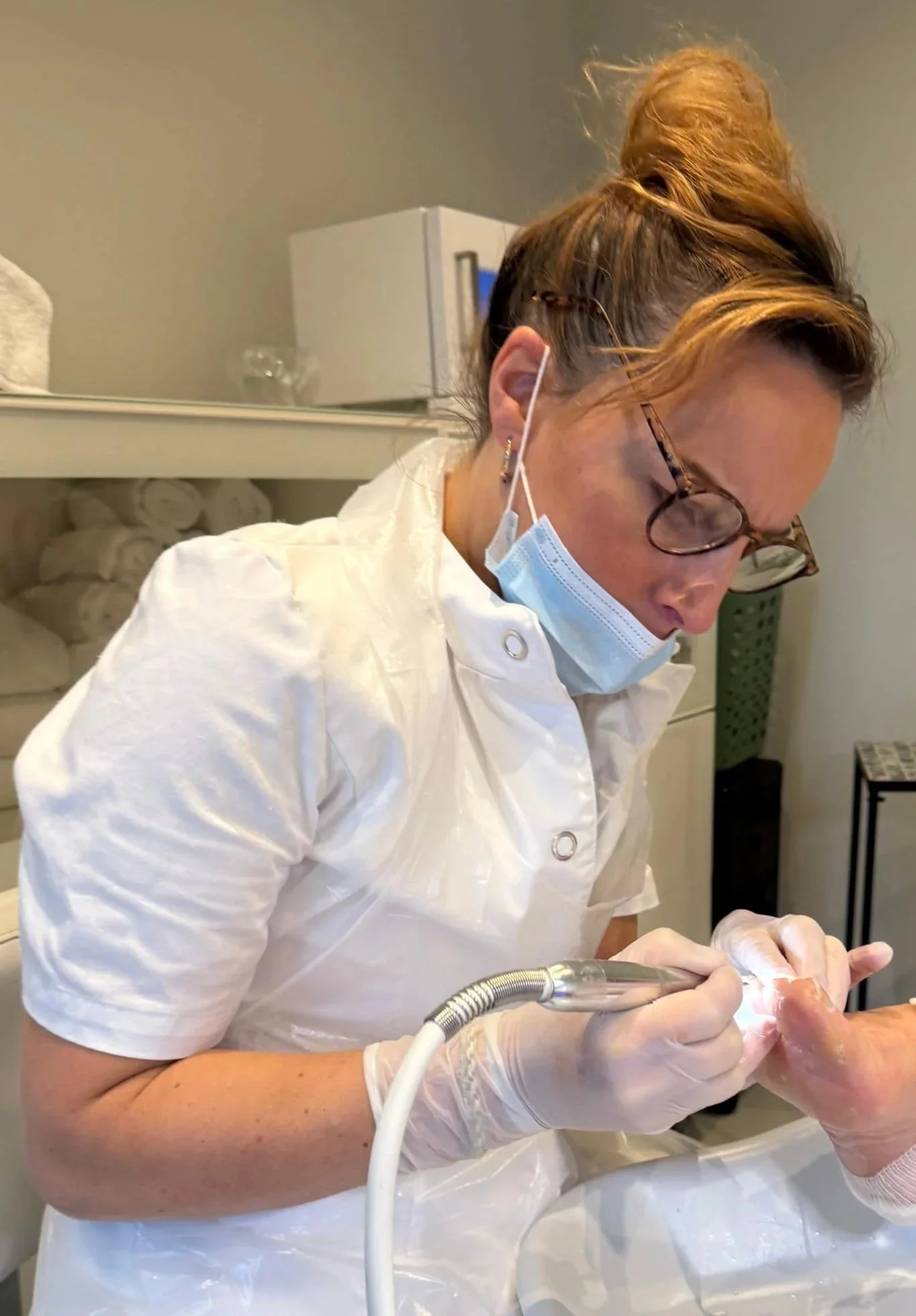 Tandarts of mondhygienist die een behandeling uitvoert in een kliniek, met een masker, brillen, witte jas, handschoenen, en een instrument.