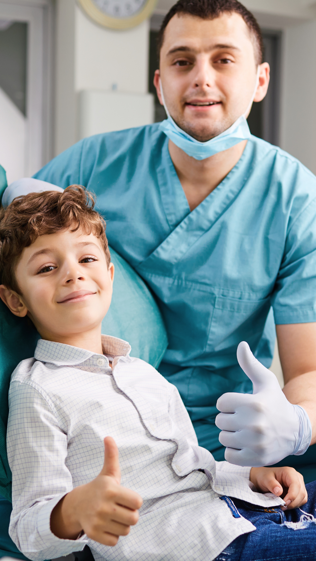 A young boy sits confidently in a hospital chair, giving a thumbs-up while a healthcare worker in blue scrubs, wearing a face mask pulled down, also shows a thumbs-up. The setting appears to be a medical facility.